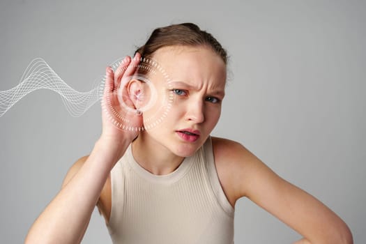 A young woman looks puzzled while leaning in with her hand on her ear. Surrounding her are visual representations of sound waves, indicating she's trying to hear better.