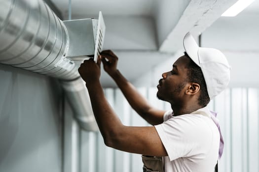 A young man is focused on fixing a ventilation duct while wearing a cap. The setting appears to be an indoor workspace, highlighting his skill and dedication.