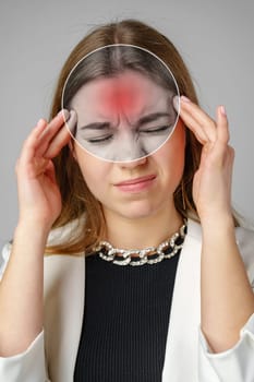 A woman is visibly in discomfort, touching her forehead with both hands while using a transparent overlay to emphasize her headache in a neutral studio environment.