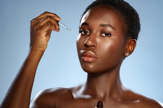 A woman with short hair holds a dropper above her face, applying serum. She gazes confidently at the camera, set against a smooth pastel backdrop, showcasing a moment of self-care.
