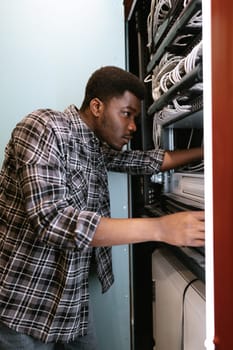 A technician is focused on adjusting equipment inside a server rack. The environment is well-lit, showcasing cables and tech gear typical of a network operations center.