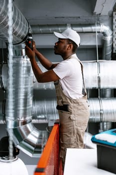 Skilled technician adjusts a ventilation duct in a modern commercial space. The worker wears light-colored overalls and a cap while ensuring air systems function properly.