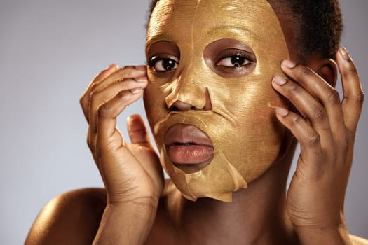 A woman gently applies a gold facial mask to her face, emphasizing the importance of skincare and self-care. The neutral background highlights her focused expression and beauty routine.