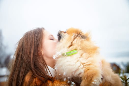 A young woman shares a joyful moment of affection with her fluffy Pomeranian in a snowy landscape.