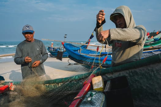 Asian Vietnamese male fishermen check fishing nets in a boat on the beach by sea in Asia. Tam Thanh, Quang Nam province, Vietnam - April 10, 2025