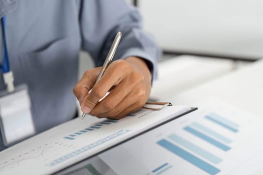 A business professional writing notes on a document filled with graphs, illustrating data analysis and strategic planning.