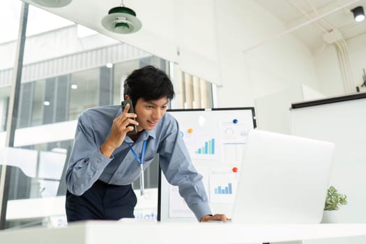 A focused businessman speaks on the phone while analyzing data on a laptop, showcasing productivity in a modern office.