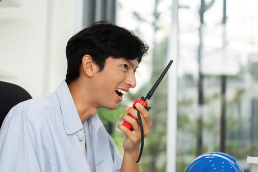 A young man enthusiastically communicating via walkie-talkie in a modern office, showcasing teamwork and effective communication.