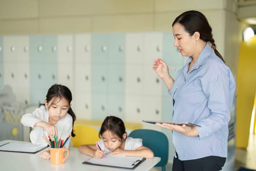 A teacher assists two young girls with their creative tasks, promoting a vibrant learning atmosphere in a classroom.
