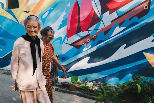 Elderly old Asian Vietnamese women on graffiti wall background in Murals Paintings Fishing Village Tam Thanh in Vietnam. Tam Thanh, Quang Nam province, Vietnam - April 10, 2025