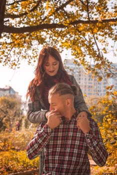 A couple in love in an autumn park, sitting on a bench, talking, laughing and holding hands. General plan. The guy kisses the girl's hand. They look at each other. Golden autumn all around.