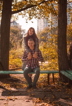 A couple in love in an autumn park, sitting on a bench, hugging and holding hands. General plan. A young couple looking at the camera.