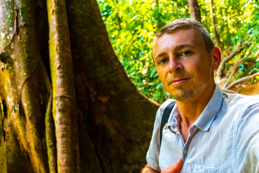Man male handsome tourist takes selfie with huge giant Canopy tree with buttress roots in Khao Lak Amphoe Takua Pa Phang Nga Thailand in Southeast Asia.