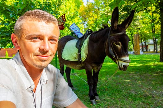 Man handsome tourist with donkey with saddle in the green park in Leninskiy Rayon Brest Brest District Brest Region Belarus.