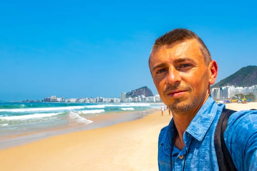 Male handsome Tourist Takes Selfie on Copacabana Beach Tropical Paradise with Blue Turquoise Water Palm Trees and White Beach Sand in Rio de Janeiro State of Rio de Janeiro Brazil.