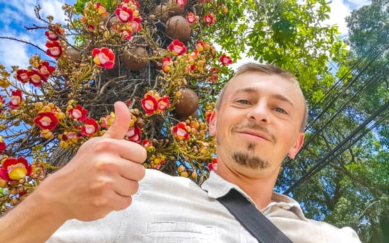 Handsome man tourist thumb up at a Cannonball tree Shorea Robusta flower tree with flowers and brown fruits in Rio de Janeiro State of Rio de Janeiro Brazil.