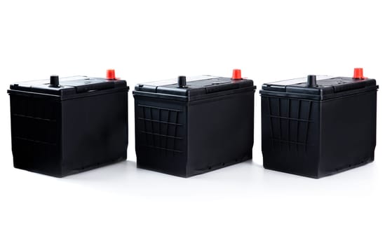 Three identical black car batteries in a row on white background. Isolated automotive parts for passenger vehicle repair, catalog, or store use.