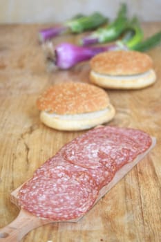 Thin slices of dry-cured salami on a wooden board with fresh bread and green onions.