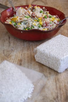 Colorful rice salad with fresh vegetables and uncooked rice on a wooden table, highlighting natural ingredients and healthy eating.