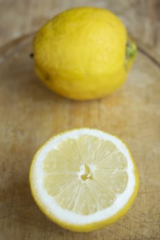 Two bright yellow lemons, one whole and one halved to reveal its juicy interior, on a rustic wooden surface