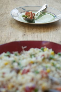 A vibrant vegetable rice salad with peas, corn, and tomatoes, surrounded by fresh ingredients on a rustic wooden surface