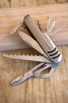 A versatile silver multi-tool knife with several blades and tools extended, lying on a textured wooden surface