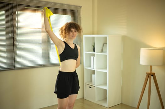 Young woman does an upper-body stretch with a resistance band in living room.