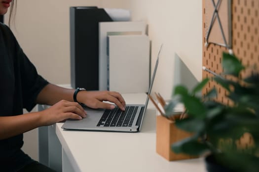Side view of young woman working on a laptop in a tidy home office.