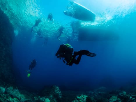 divers diving towards the boats on the sea surface, concept of scuba diving and underwater adventure