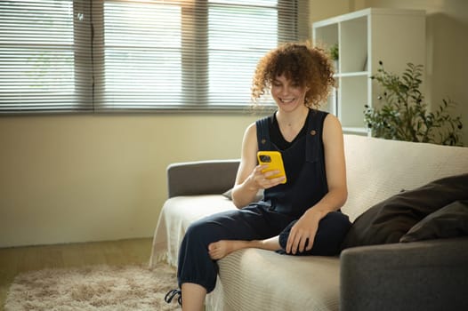 Relaxed young woman smiles while using her smartphone on a cozy couch.