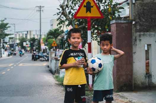 Two Asian Vietnamese child boys soccer player with a football ball on the street in village. Tam Thanh, Quang Nam province, Vietnam - April 10, 2025