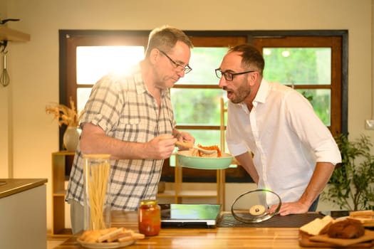 Cheerful mature father and adult son enjoy preparing a homemade meal together.