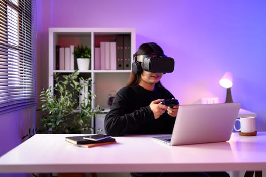 Woman wearing a VR headset and headphones plays with a controller at a desk.