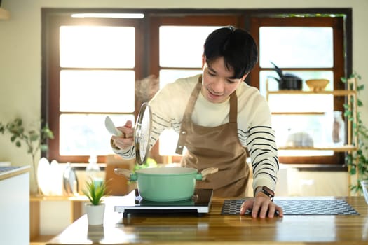 Smiling man in an apron preparing meal in a sunlit modern kitchen.