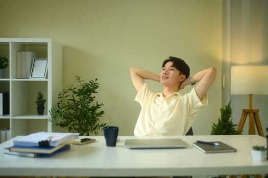Casual man leaning back in his chair with hands behind head, in a bright home office.