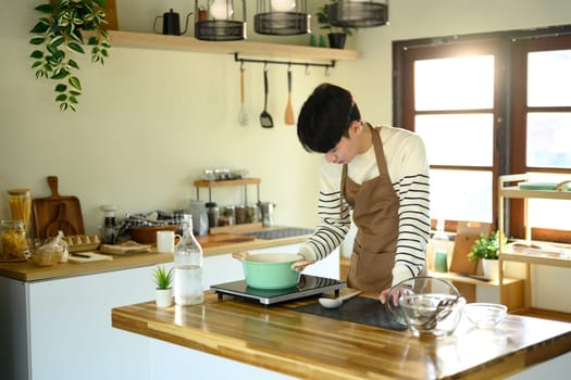 Smiling man in an apron preparing meal in a sunlit modern kitchen.