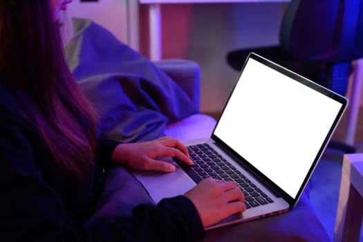 Woman types on laptop with white display, surrounded by colorful ambient lighting.