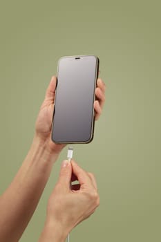 female hand plugging charger cord into smartphone to charge battery on green background, Wired charging