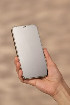woman holding smartphone with blank screen on beige background, mockup