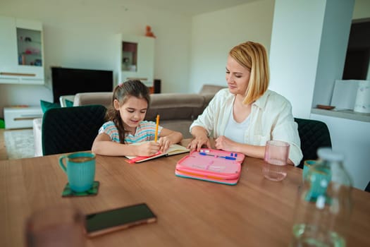 A mother guides her daughter while she writes in a notebook.