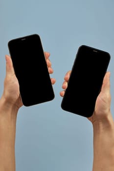 woman holding two smartphones with blank screens on blue background