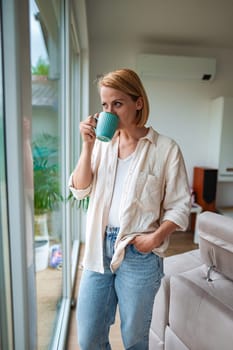 Woman enjoys a warm drink while gazing out the window.