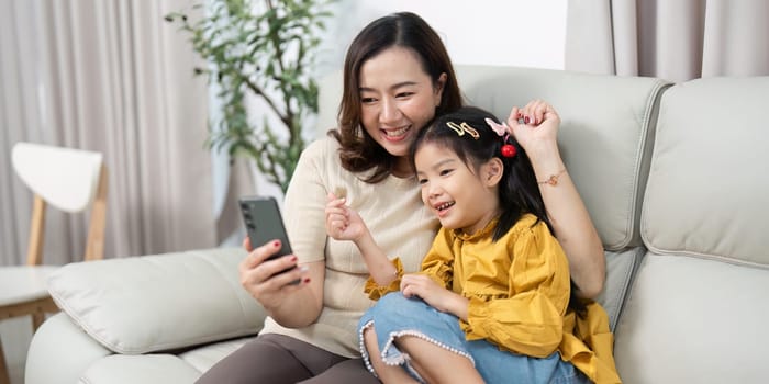 The mother and daughter enjoy a fun moment together, exploring content on a smartphone, highlighting their joyful family dynamic.