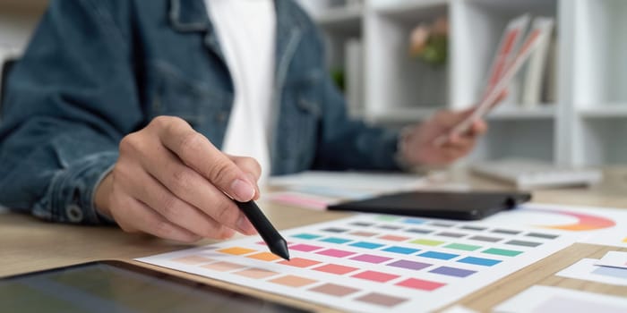 A designer carefully analyzes color schemes and layouts using swatches and a digital tablet in a stylish workspace.