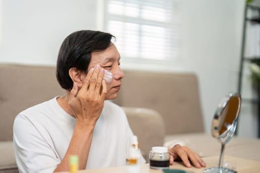 A senior man takes time for his skincare, applying products thoughtfully in front of a mirror, emphasizing the importance of self-care for aging skin.