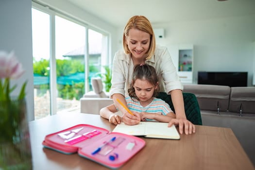 A mother guides her daughter as they study together happily.