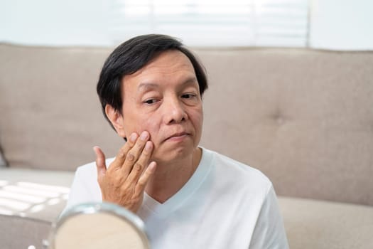 An elderly man applies skincare products to his face, focusing on maintaining healthy skin and enjoying a self-care moment in a peaceful home setting.