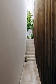 A narrow and winding alleyway that features stairs leading upwards, alongside a wellmaintained wooden fence for added charm and character