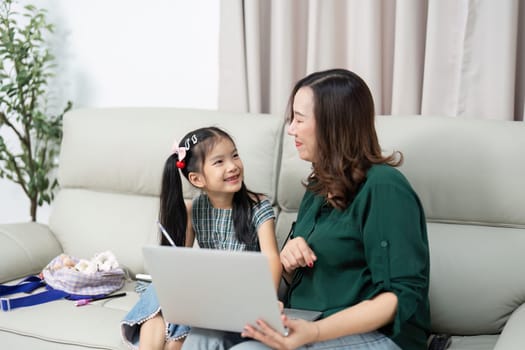 A mother and her daughter sit together on a couch, engaging in a learning activity on a laptop. This image captures the essence of back-to-school preparations and family support.