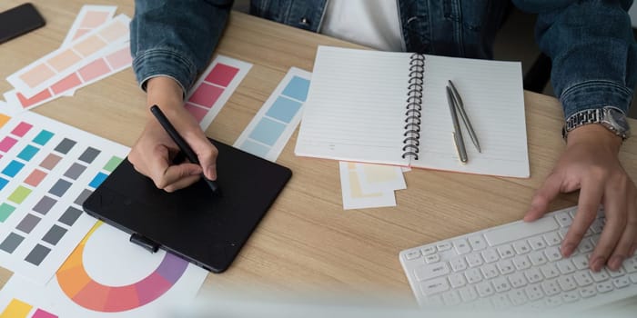 A designer engages in the creative process, using a digital tablet and color swatches to develop visual concepts in a modern workspace.